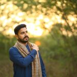 A man in a blue shirt and scarf enjoying a serene outdoor setting in natural sunlight.